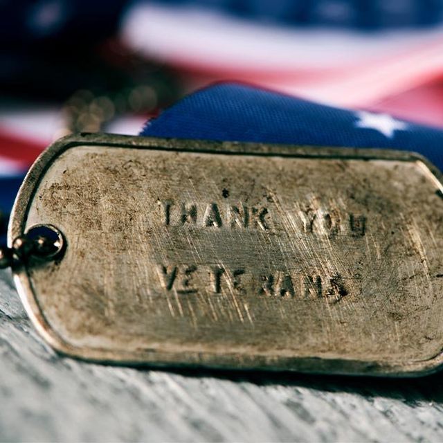 A military dog tag stamped Thank You Veterans resting on an American flag