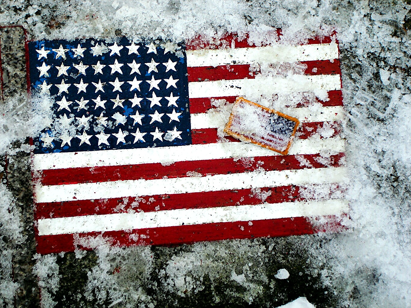 The weathered American flag painted on the memorial stone, dusted with snow